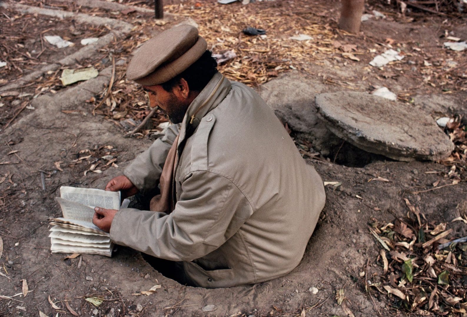 00418_05. Man reads a book from a hole in the ground.