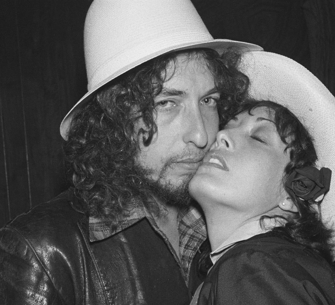 The Day I Shook The Hand Of Bob Dylan 1976: Actress/singer Ronee Blakley knew I was a huge Bob Dylan fan. I lucked out and obtained first row tickets at his 1974 Los Angeles concert. I sold my first photograph from this show and it was the start of my wonderful photo career. Ronee was performing at the Roxy and told me Bob was coming to the second set. He sat in the VIP section and was escorted backstage. Ronee got me back there and introduced me to Dylan. He was very friendly, remarking that I looked a bit like him. He gave me a really limp handshake that was not too impressive. Ronee grabbed him and we did this amazing set of photographs. I was in heaven. After this set, Bob set up another group shot of him with a new actor named Robert De Niro and other friends, including musician David Blue, actress/singer Lanie Kazan, actresses Martine Getty and Sally Kirkland. I did not have a clue who any of these folks were, but sold the shot to "People" and "Rolling Stone," to name just a few.